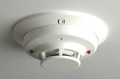 Can the smoke sensors in a home security/fire alarm system replace the smoke alarms required by the building code?